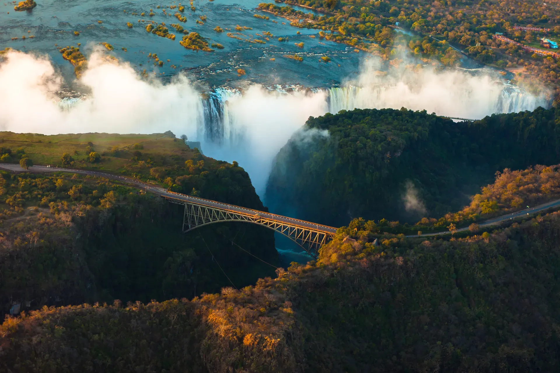 Aerial view of a waterfall plunging into a gorge with lush forest and an adventurous walkway along the edge